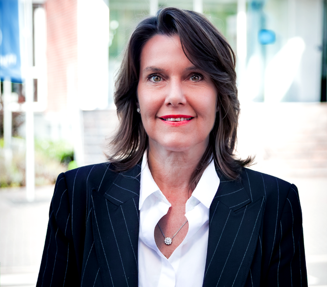 Frau, braune Haare, lächelnd, trägt eine weiße Bluse 