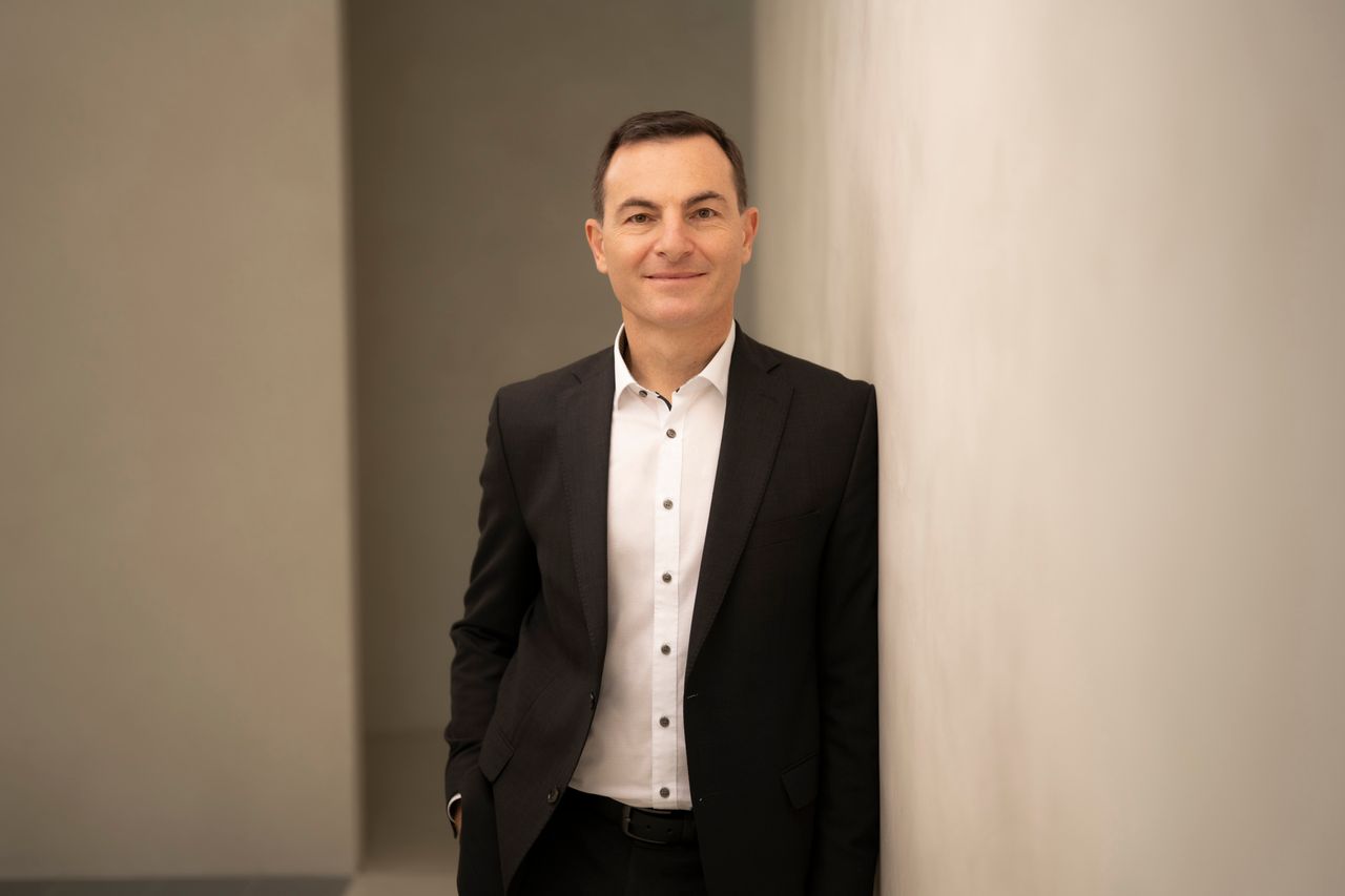 Man in a black suit, with a white shirt, smiling