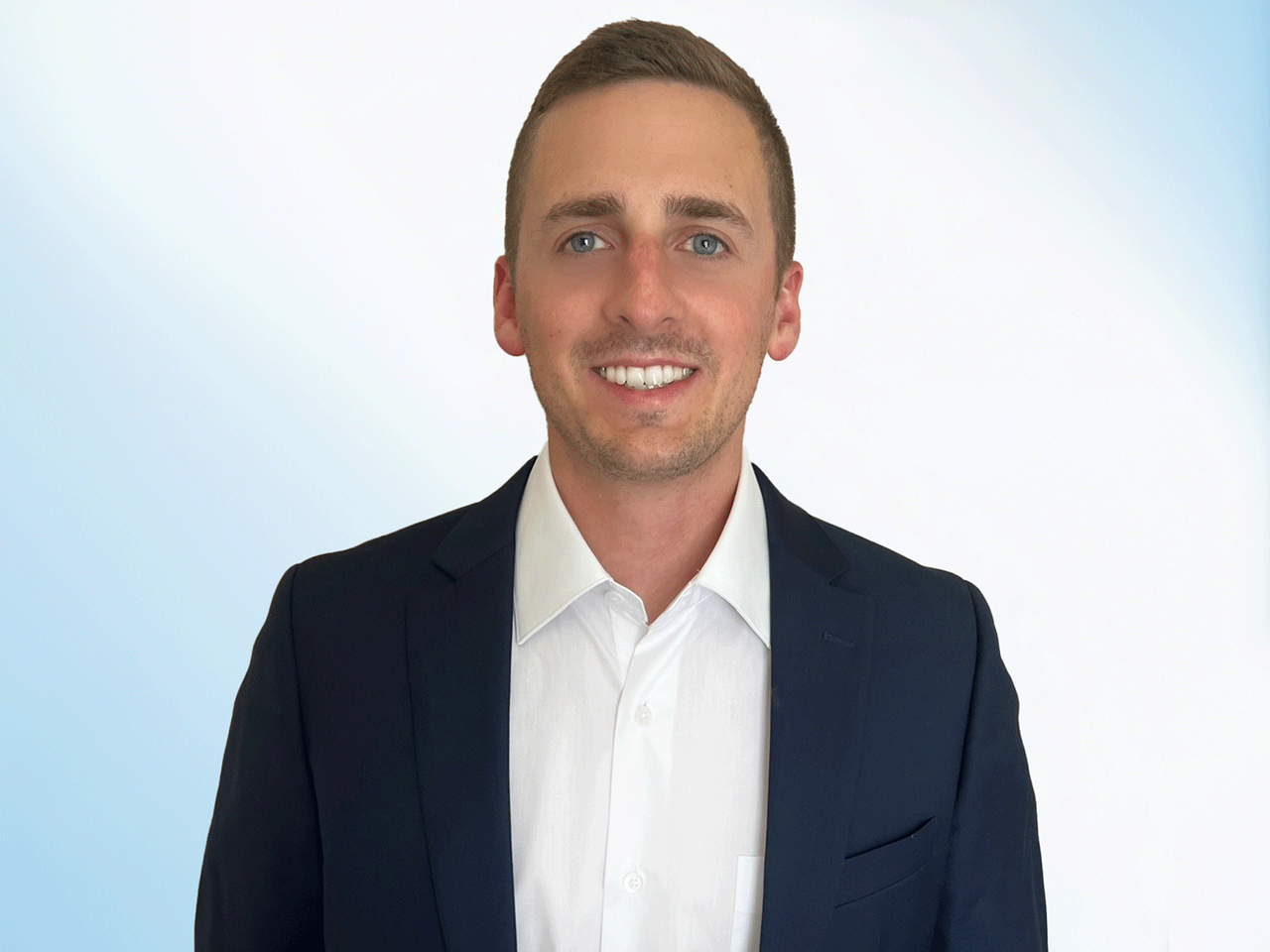 Man in a suit smiling, in front of a white/blue backdrop