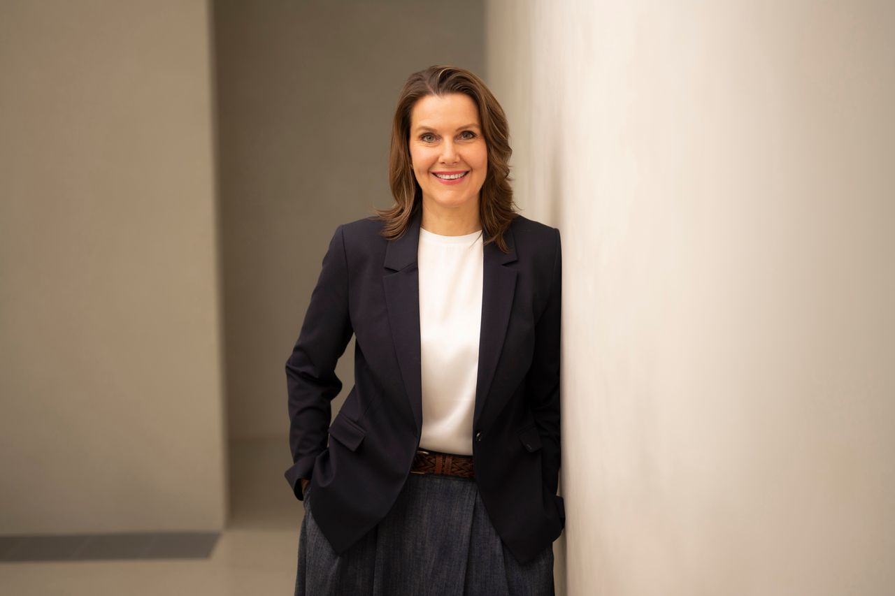 Woman, brown hair, smiling, wearing a white blouse and a black blazer