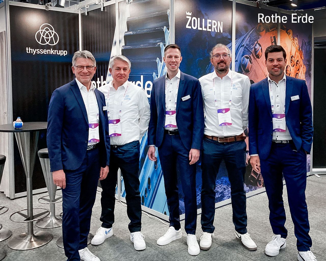 Five men in suits, standing in front of booth wall