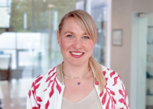 Femme blonde, cheveux attachés en chignon, souriante, portant un t-shirt avec un imprimé noir et blanc.