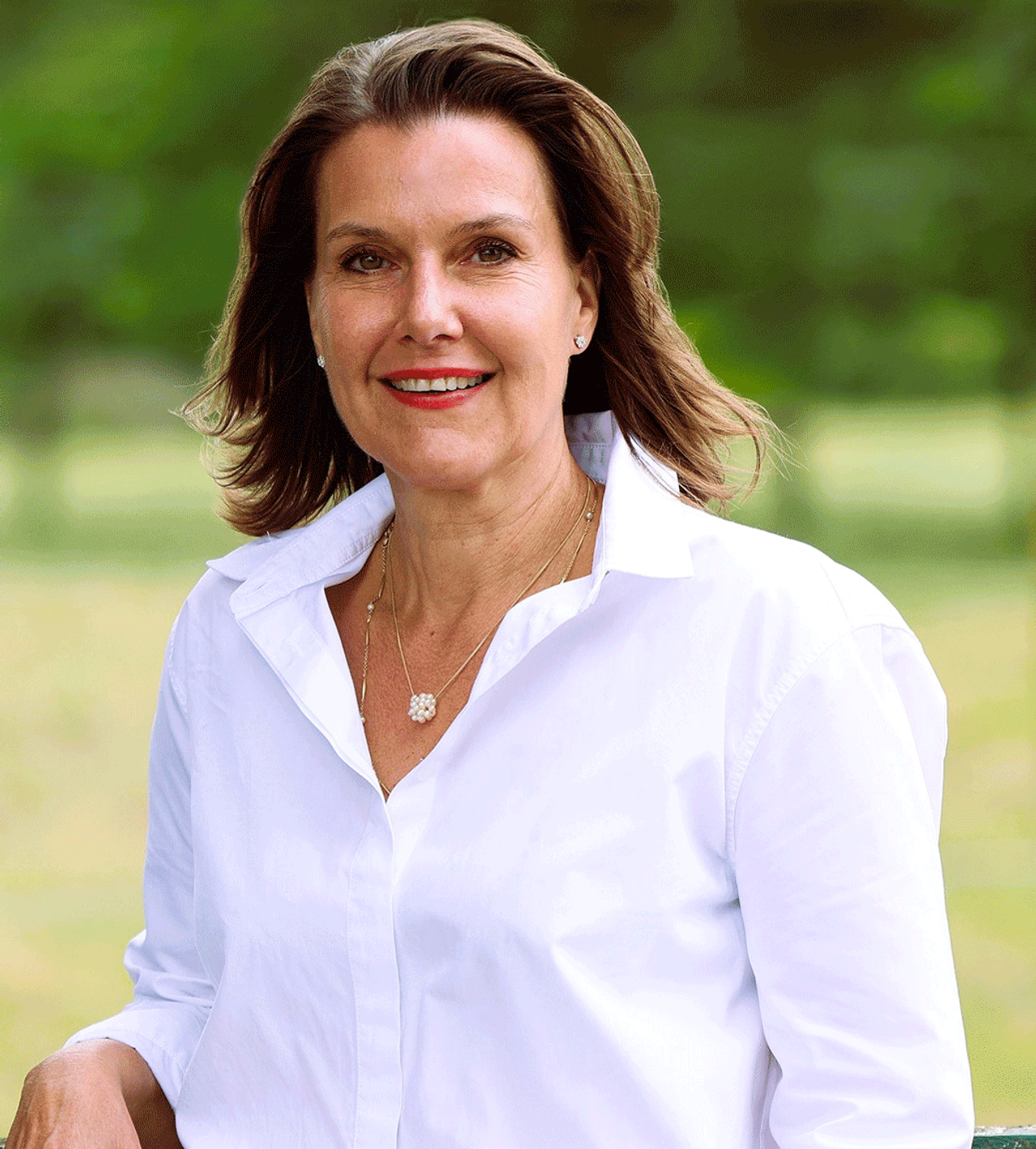 Žena s hnedými vlasmi, úsmevom, oblečená v bielej blúzke