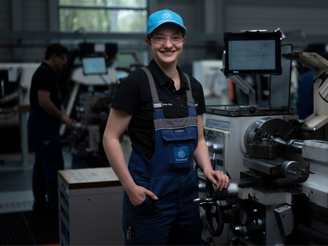 Junge Frau an einer Drehbank, mit Cap auf dem Kopf.