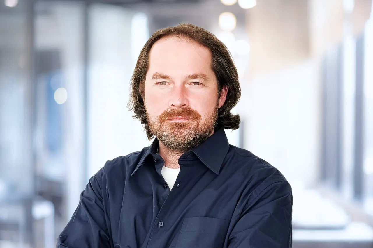 Man with shoulder length hair, beard, smiling, wearing a dark shirt