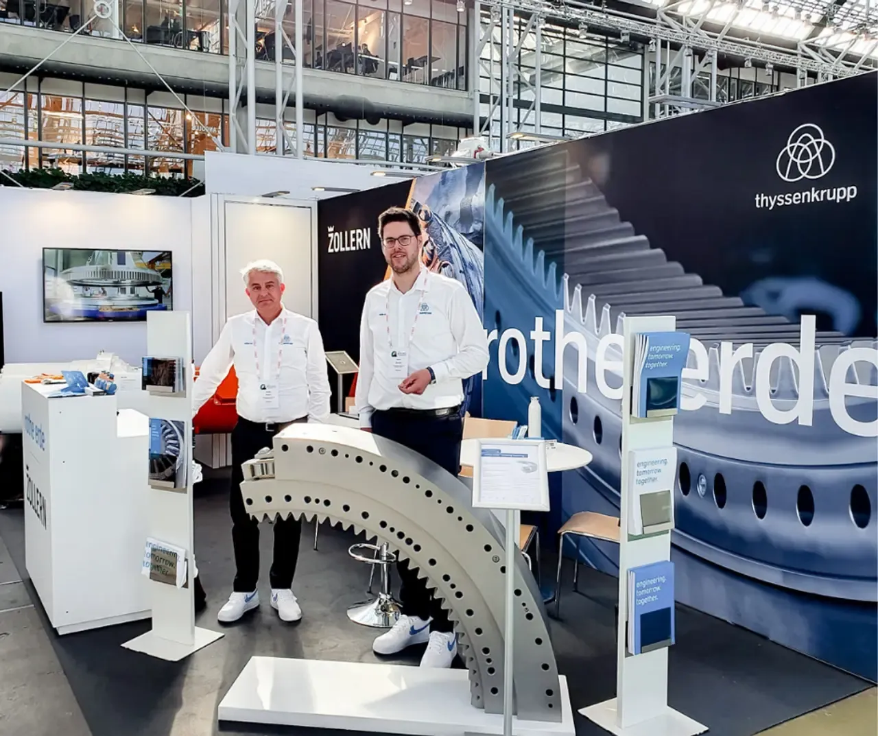 Two men in thyssenkrupp rothe erde shirts at a trade fair stand